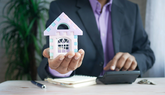A personal in formal suit holding a miniature house