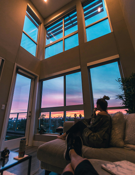 A women sitting on couch seeing sunset through her windows of her home